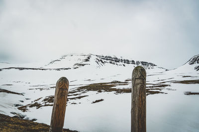 Close-up of wooden post on snow covered mountain against sky