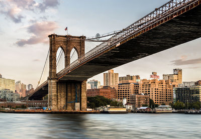 Low angle view of brooklyn bridge over river against sky in city