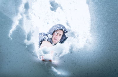 Low angle view of young man removing snow on windshield seen through car