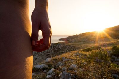 Midsection of person on shore during sunset