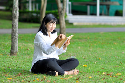 Young woman using phone while sitting on grass