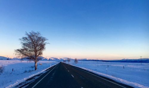 Road by snow covered landscape against blue sky