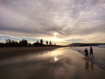 People walking on beach against sky during sunset