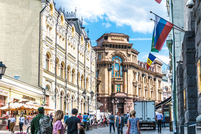 People on street amidst buildings against sky in city