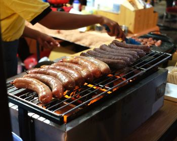 Midsection of person preparing sausage on barbecue grill