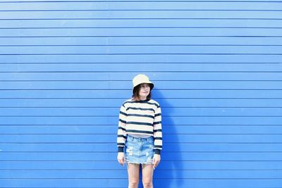 Portrait of young woman standing against blue wall