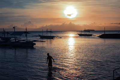 Silhouette person standing in sea against sky during sunset