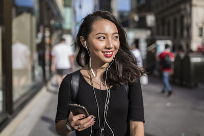 Usa, new york city, manhattan, young woman listening music with cell phone and earphones on the street