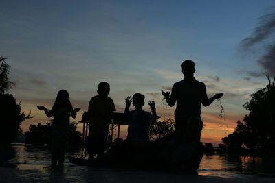 Silhouette people on lake against sky during sunset