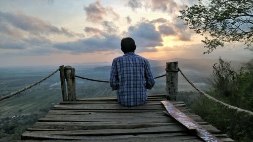 Rear view of man standing on railing against sky