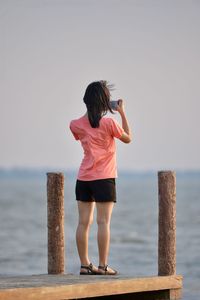 Rear view of woman standing by sea against sky