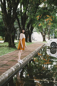 Full length of thoughtful woman standing on sidewalk by puddle