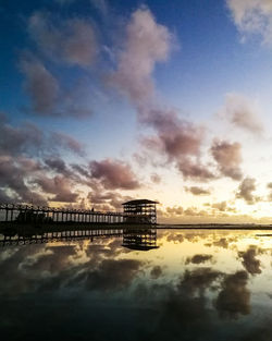 Silhouette bridge by building against sky during sunset