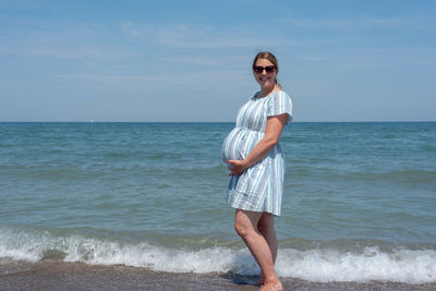 Full length of pregnant woman standing on beach against sky