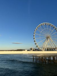 Ferris wheel by sea against clear blue sky