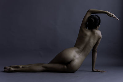 Midsection of shirtless woman against gray background