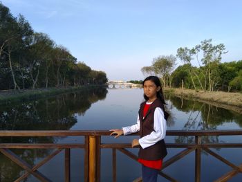 Portrait of girl standing on bridge over lake against sky