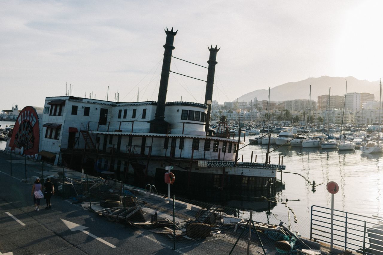 BOATS MOORED AT HARBOR BY BUILDINGS AGAINST SKY