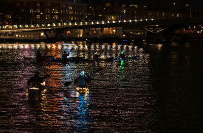 People on illuminated bridge over river in city at night