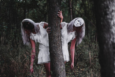 Women in masks holding tree in forest