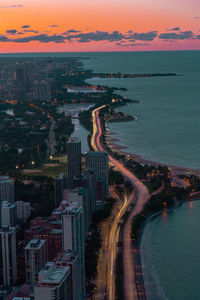 High angle view of illuminated city by sea against sky at sunset