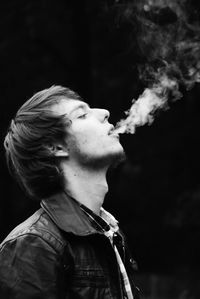 Close-up of man emitting smoke against black background