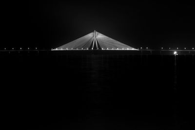 Illuminated bridge over sea against clear sky at night