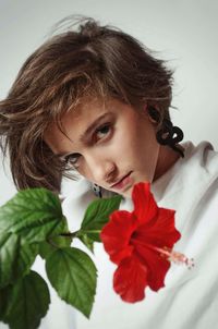 Close-up portrait serious young woman by red hibiscus against white background