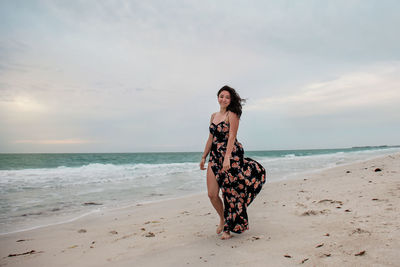 Young woman with umbrella on beach against sky