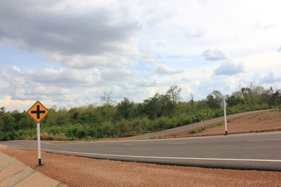 Road sign by trees against sky