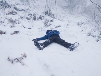 Funny boy laying in snow and makes an angel with spread arms. kid play game in snow on stony hill