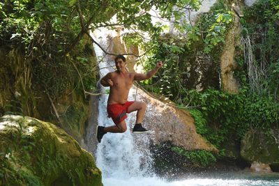 Full length of shirtless man on rock in forest