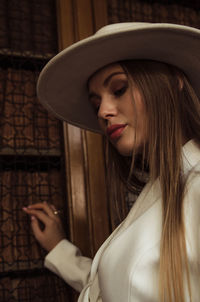 Beautiful young woman wearing hat and blazer by wall