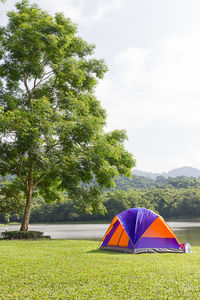 Multi colored tent on field by trees against sky