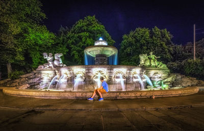 Young woman statue against trees at night