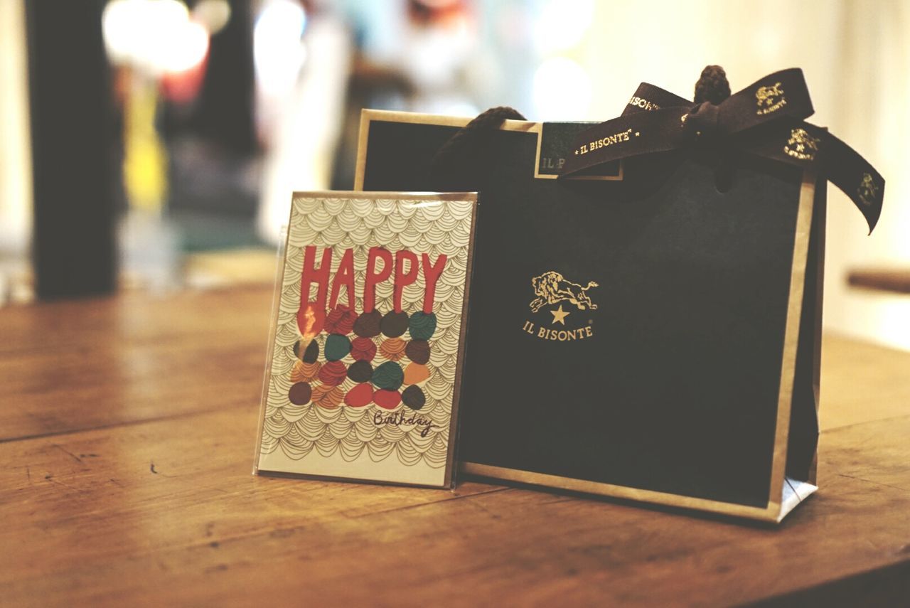 indoors, table, still life, close-up, focus on foreground, text, wood - material, communication, selective focus, decoration, art and craft, hanging, no people, paper, home interior, religion, art, creativity, western script, wooden