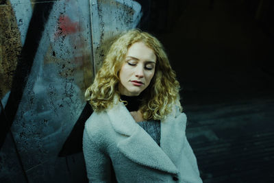 Portrait of young woman standing against wall