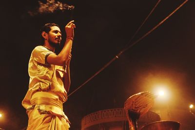 Low angle view of man holding illuminated light against sky at night