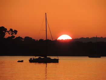 Silhouette sailboats in sea against orange sky