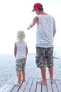 Rear view of man pointing while standing with son on jetty at beach