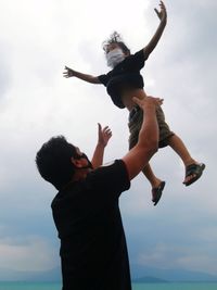 Low angle view of father tossing son mid air against sky