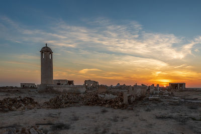 Lighthouse amidst buildings against sky during sunset