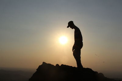 Silhouette man standing on rock against sky during sunset