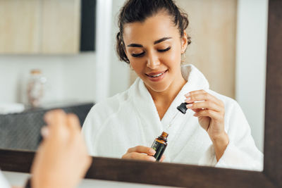 Young woman holding essential oil standing in bathroom