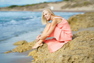 Portrait of young woman sitting on rock at beach