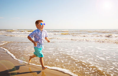 Full length of boy running at beach against sky