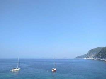 Boats on sea against clear blue sky