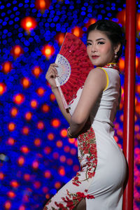 Portrait of young woman in cheongsam holding hand fan during festival