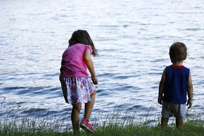 Rear view of siblings standing on grassy field against lake