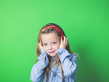 Portrait of girl listening music while standing against green background